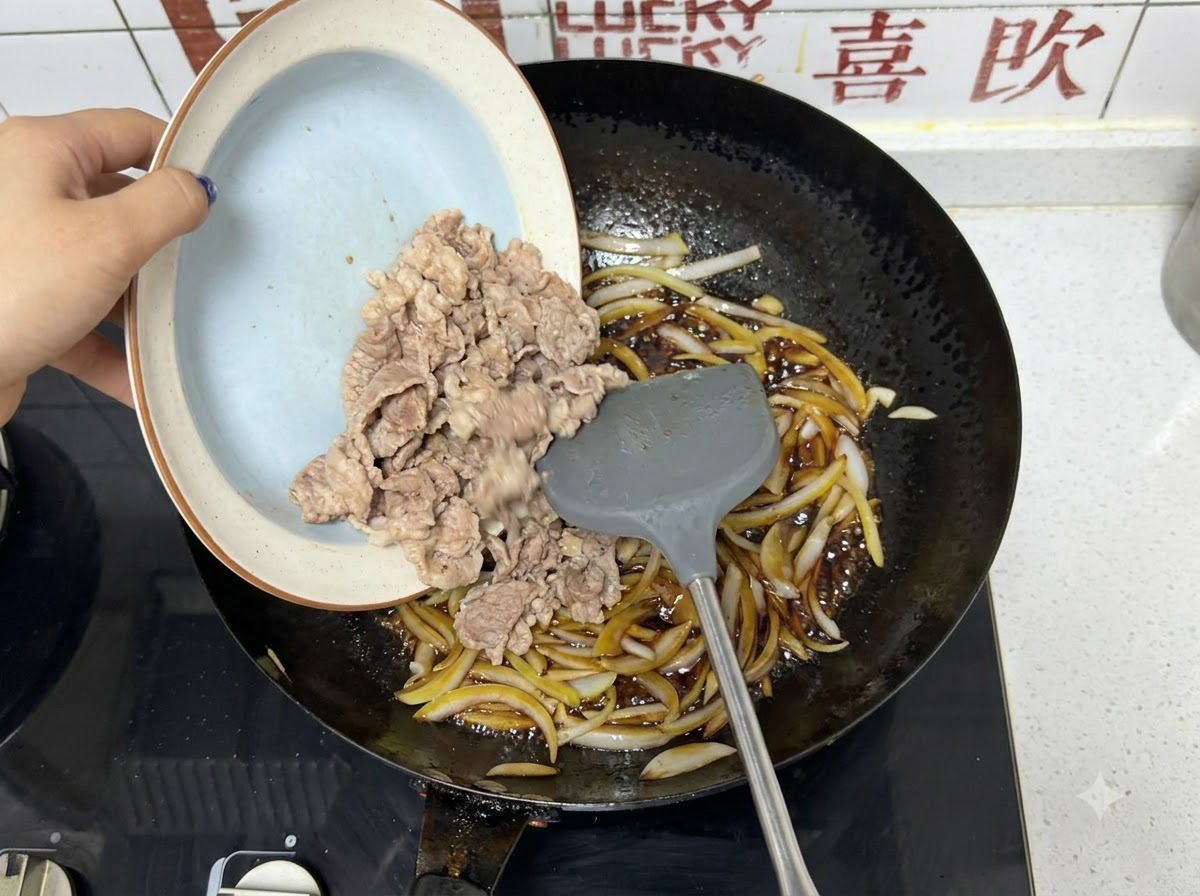 Fettine di manzo precedentemente sbollentate versate da un piatto in un wok con cipolle e salsa scura.