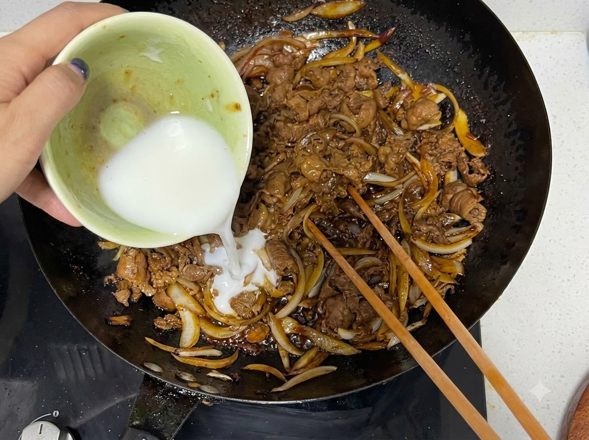 Miscela di amido di mais versata da una ciotola in un wok con manzo e cipolle cotti, accanto a bacchette di legno.
