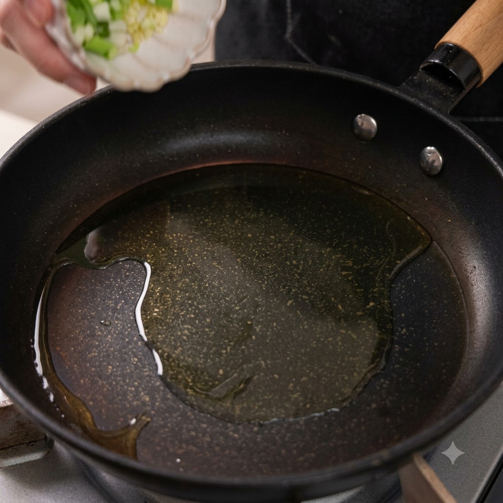 Aglio tritato e parti bianche di cipollotto che cadono in una padella con olio caldo.