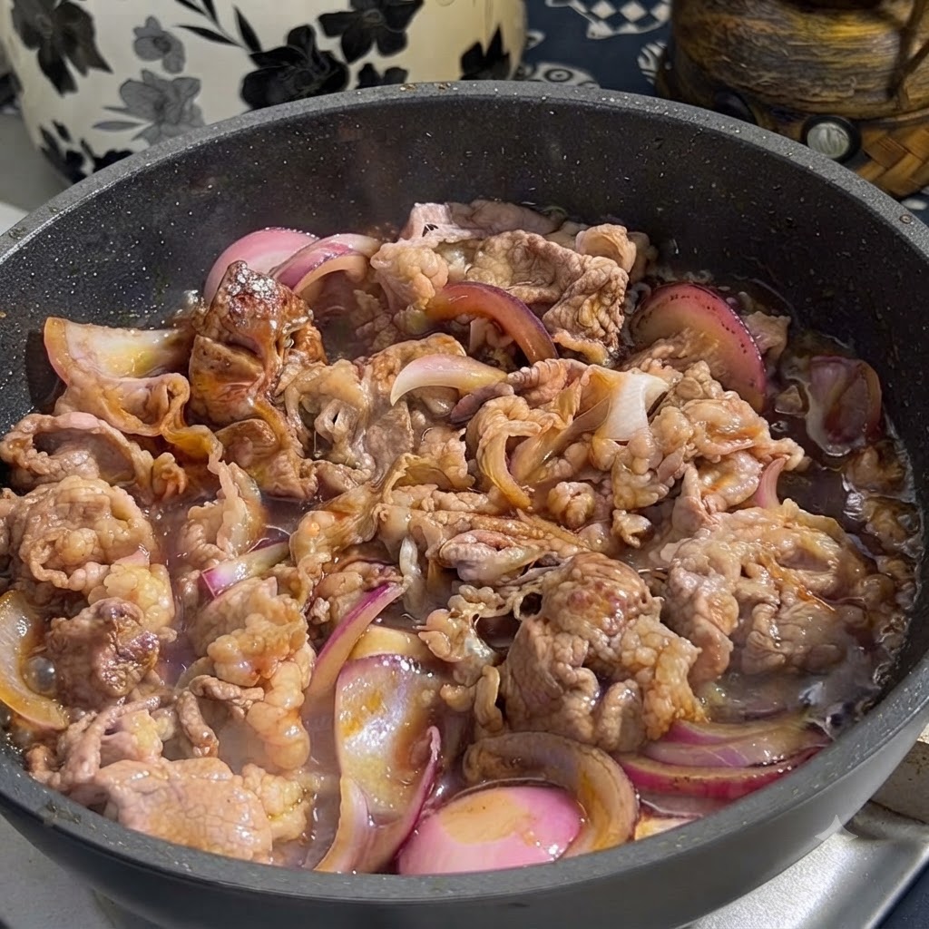 Salsa teriyaki versata da un contenitore in una padella contenente manzo dorato e cipolle rosse affettate.
