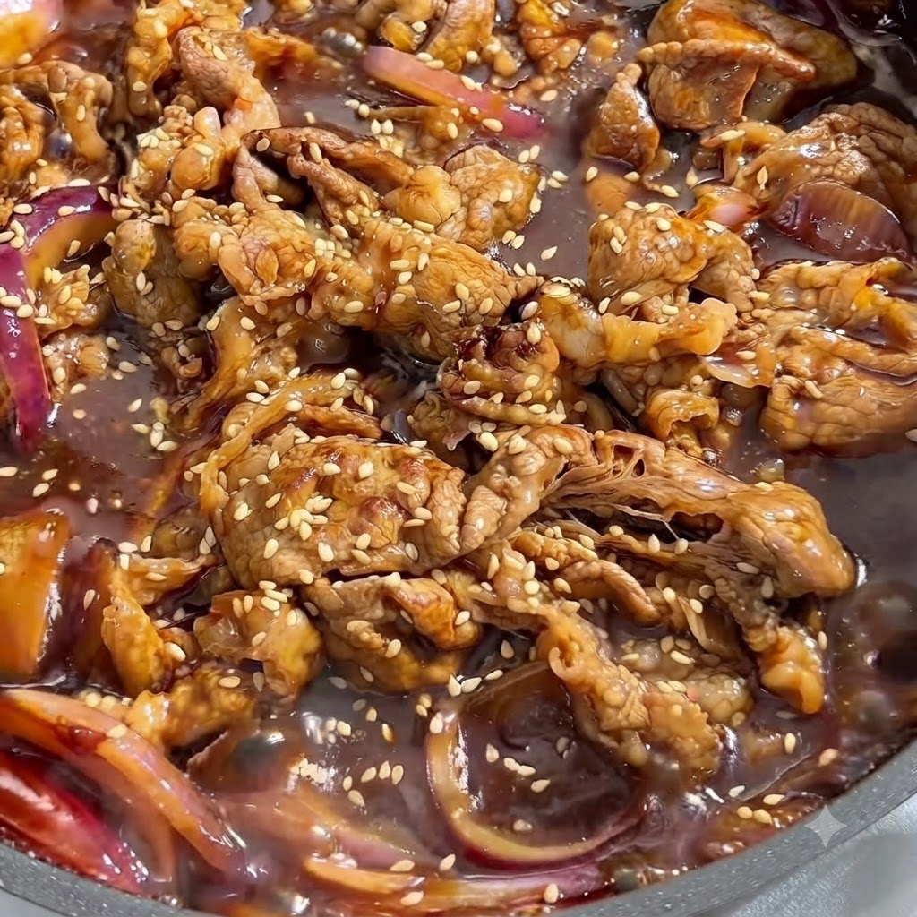 Vista ravvicinata di manzo cotto e cipolle rosse che sobbollono in una salsa scura saporita, ricoperte di semi di sesamo bianco.