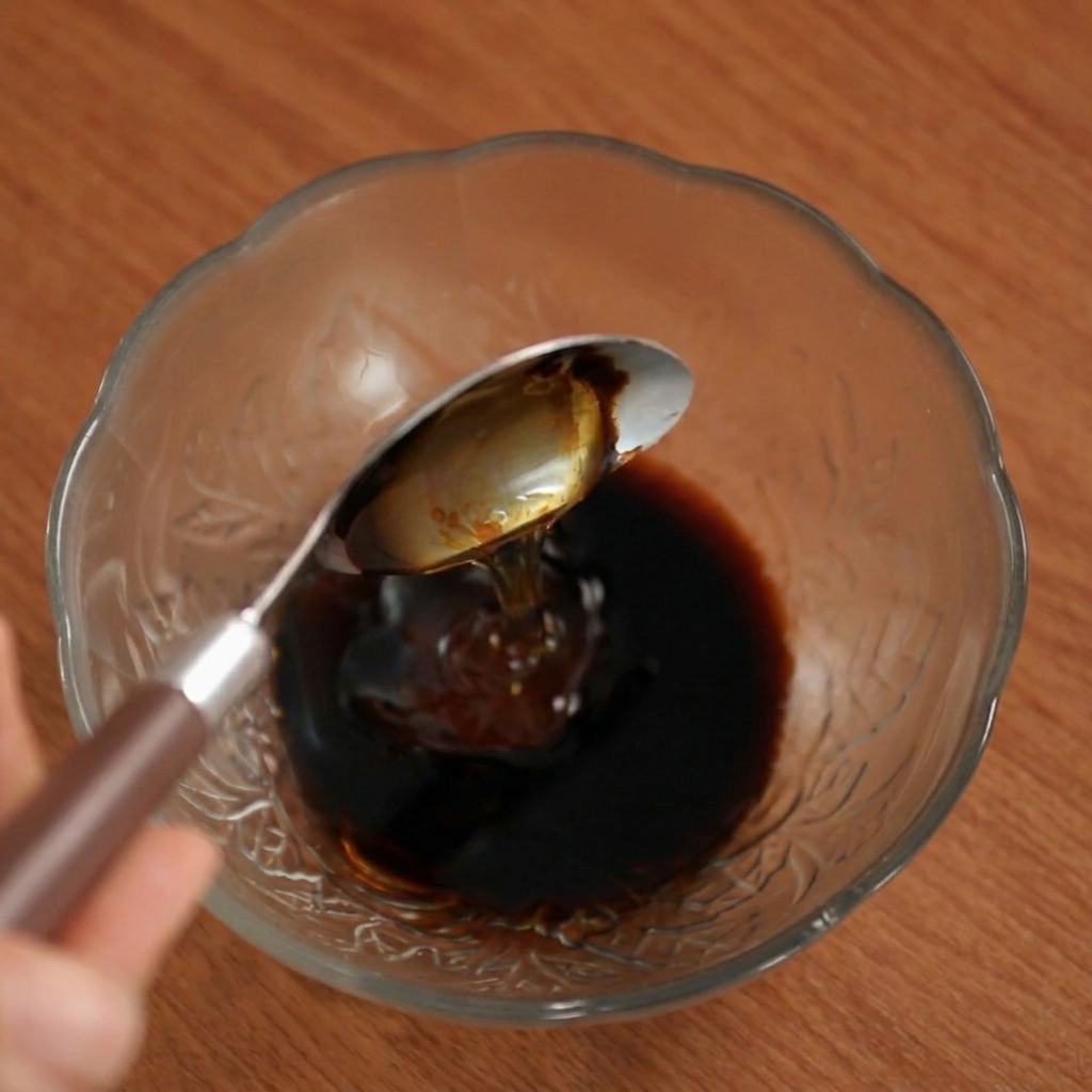 Miele versato da un cucchiaio nella miscela di salsa scura in una ciotola di vetro.