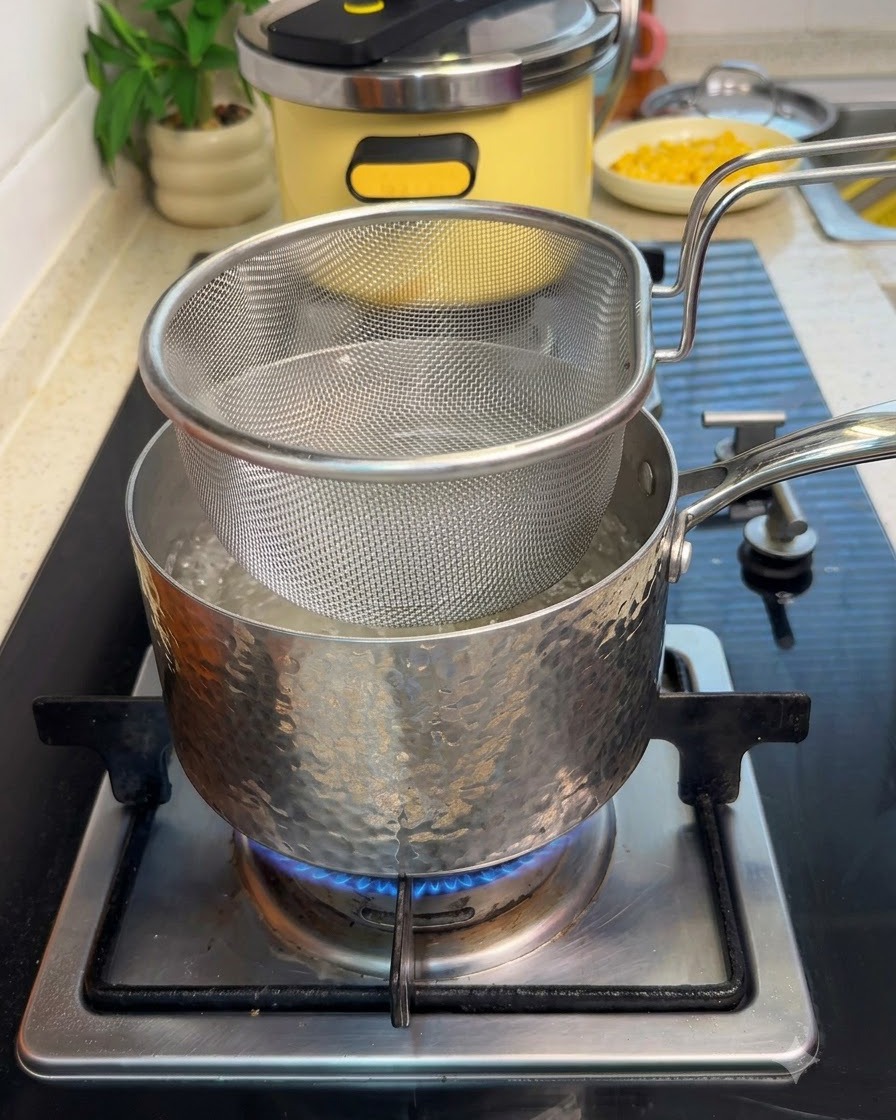 Un cestino scolapasta in rete immerso in una pentola di acqua bollente su una stufa con manzo affettato.