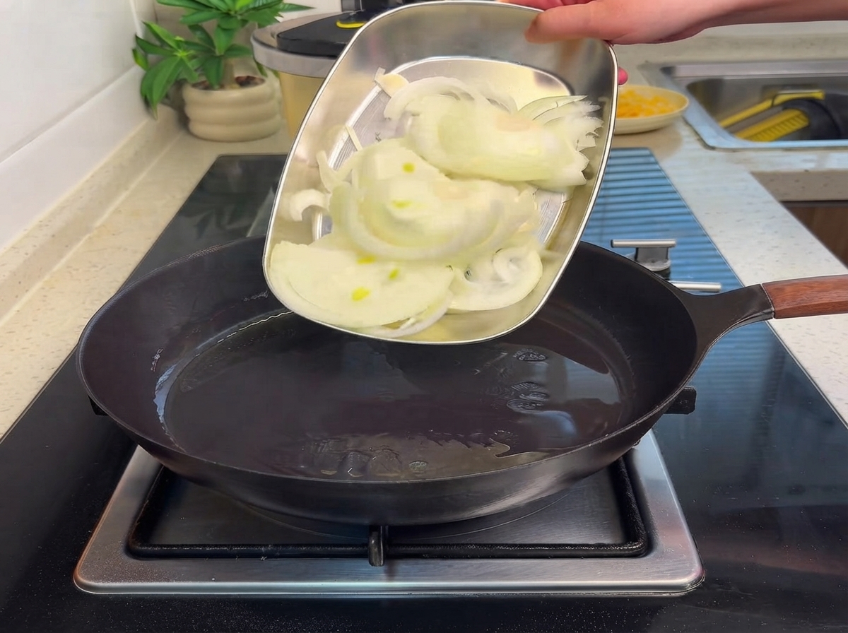Cipolle affettate fatte scivolare da un vassoio di metallo in una padella calda con olio.
