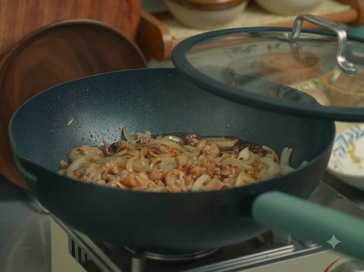 Una padella piena di manzo e cipolle coperta con un coperchio di vetro su un piano cottura.