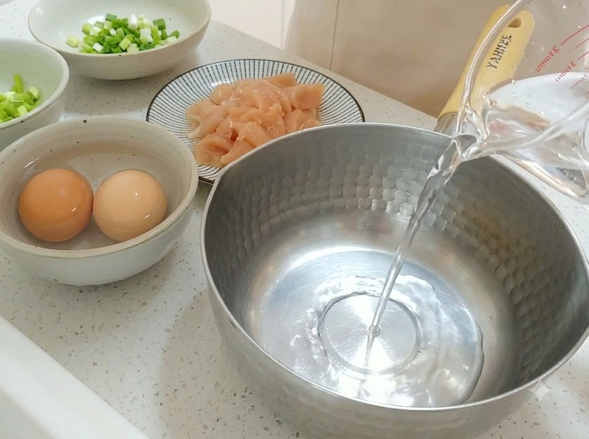 Acqua pulita versata da un misurino in una pentola di acciaio inossidabile.