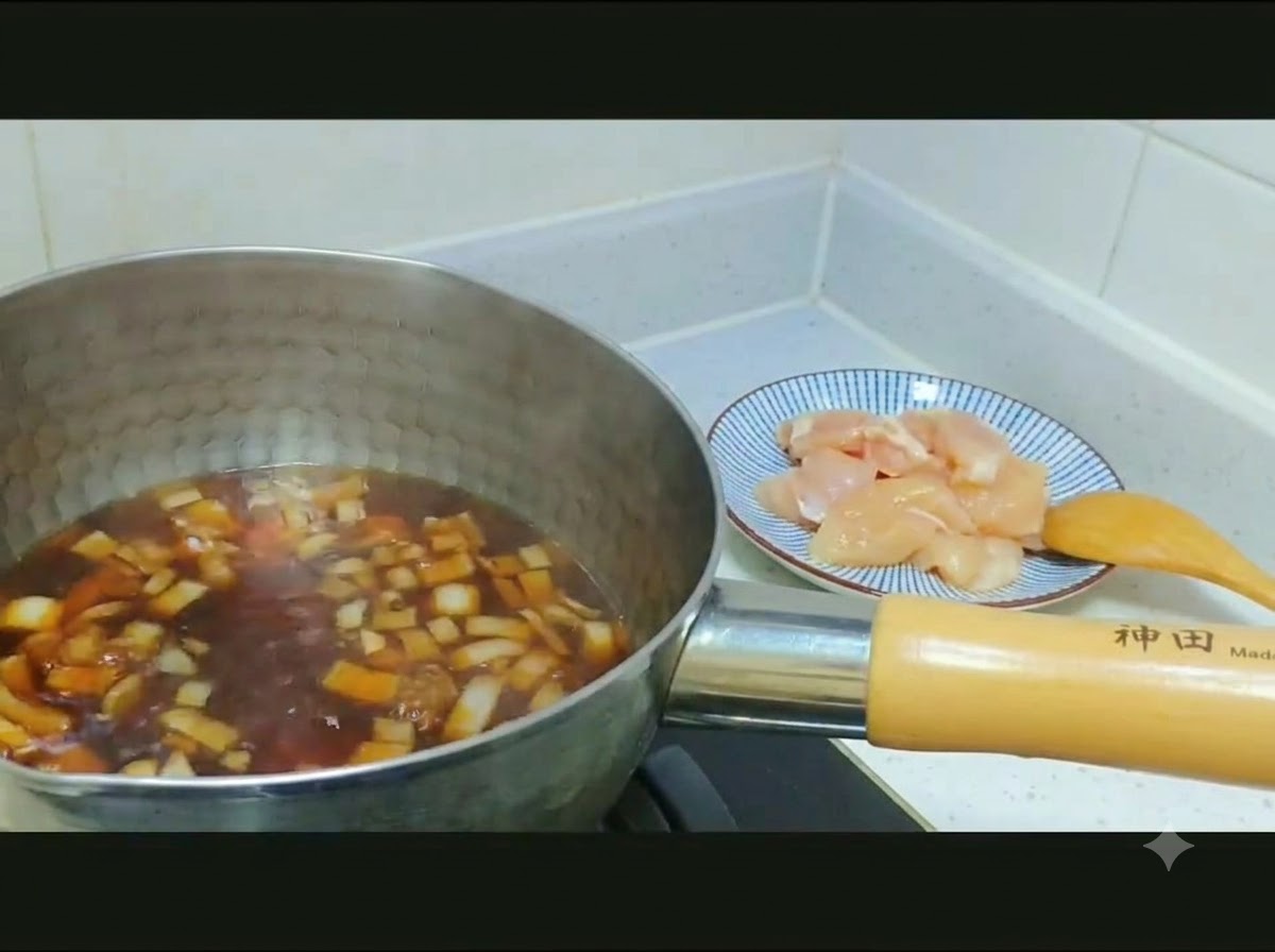 Pollo a cubetti crudo e cipolle affettate trasferiti da un piatto decorato in una pentola di brodo scuro.