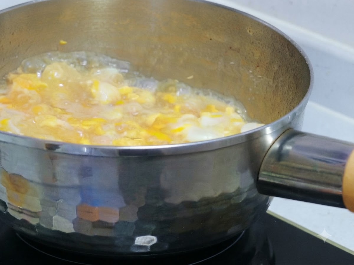 Liquido di uovo parzialmente sbattuto versato su pollo e cipolle che sobbollono in una pentola.