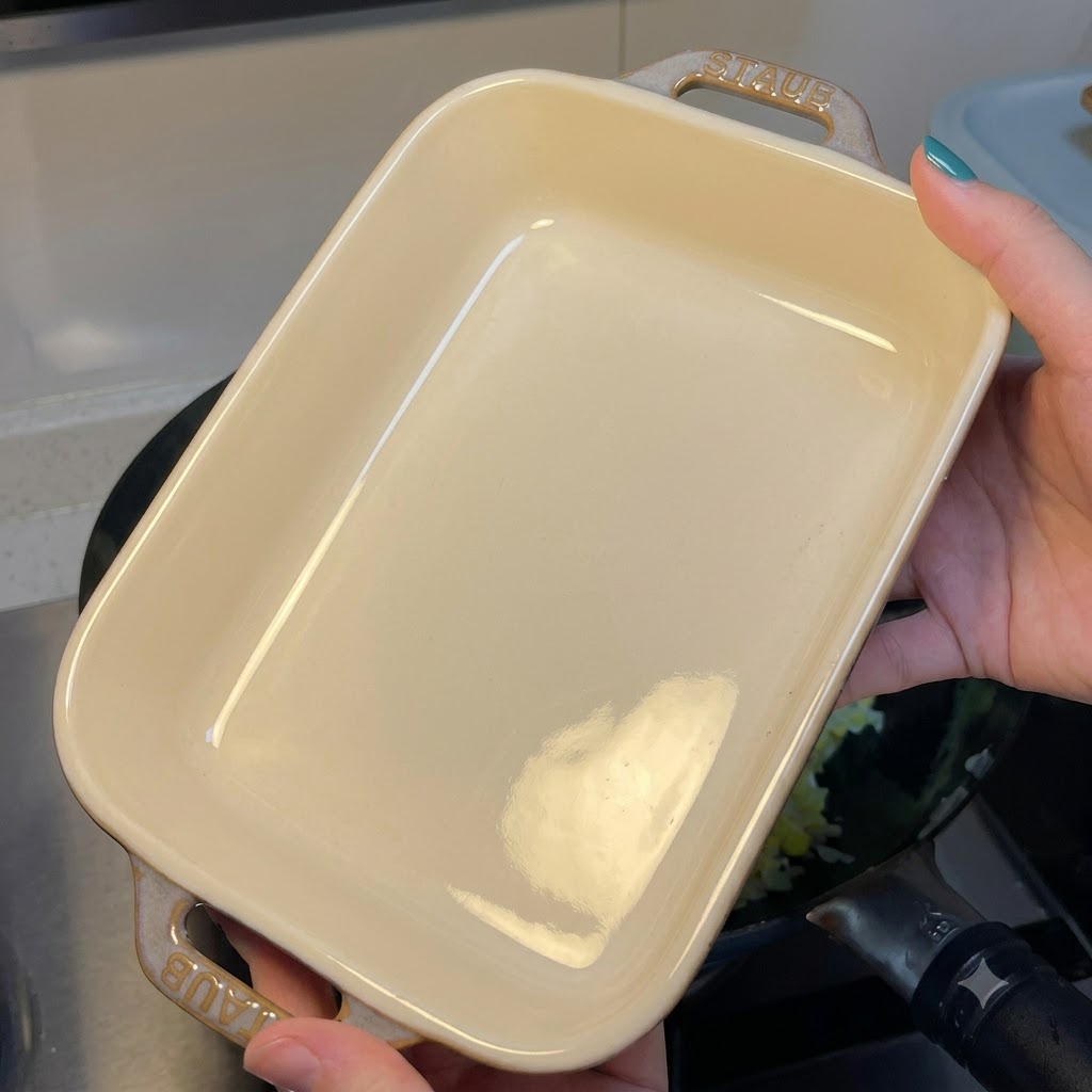 Una persona tiene una pirofila rettangolare in ceramica bianca sopra un wok contenente riso saltato con uova.