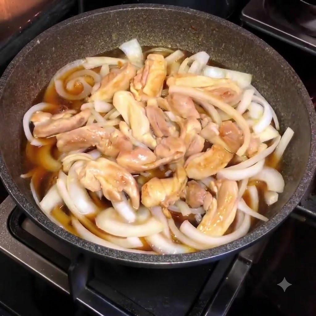 Una padella piena di cipolle affettate, pezzi di pollo e salsa marrone, vista dallalto durante il processo di cottura a fuoco lento.