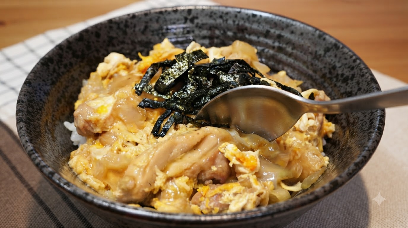 Una confortante ciotola di Oyakodon giapponese con pollo tenero, uova setose e alga nori sminuzzata su riso bianco al vapore.