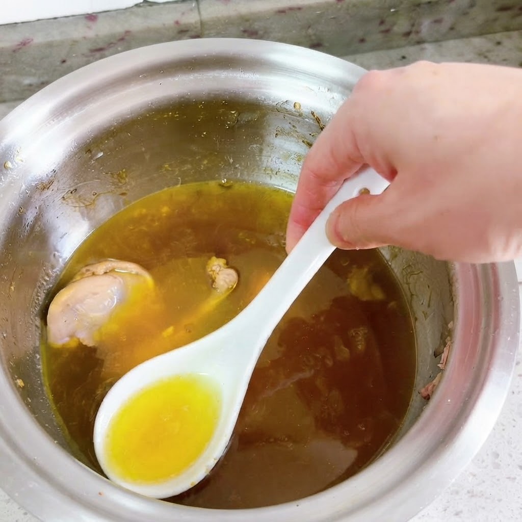 Un cucchiaio bianco che rimuove lolio giallo brillante dalla superficie di una zuppa danatra in ebollizione.