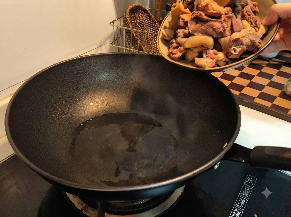 Una mano che versa pezzi di anatra sbollentata da un piatto in un wok nero caldo con olio.