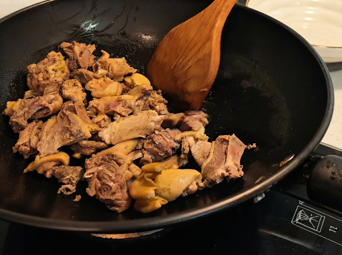 Pezzi di anatra saltati in un wok con una spatola di legno, con la pelle dorata.