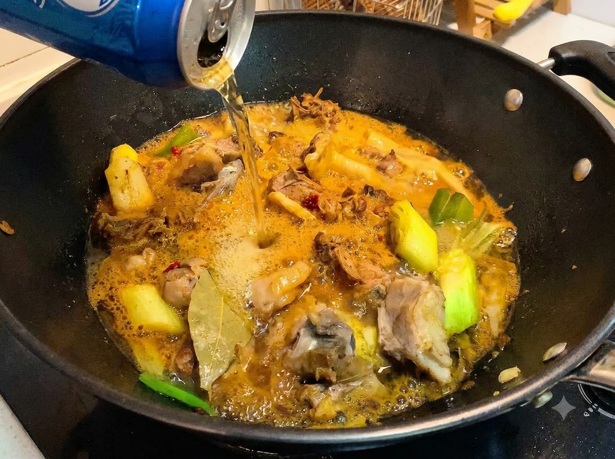 Una lattina di birra versata in un wok contenente pezzi di anatra cotta e una salsa ricca e spumeggiante.