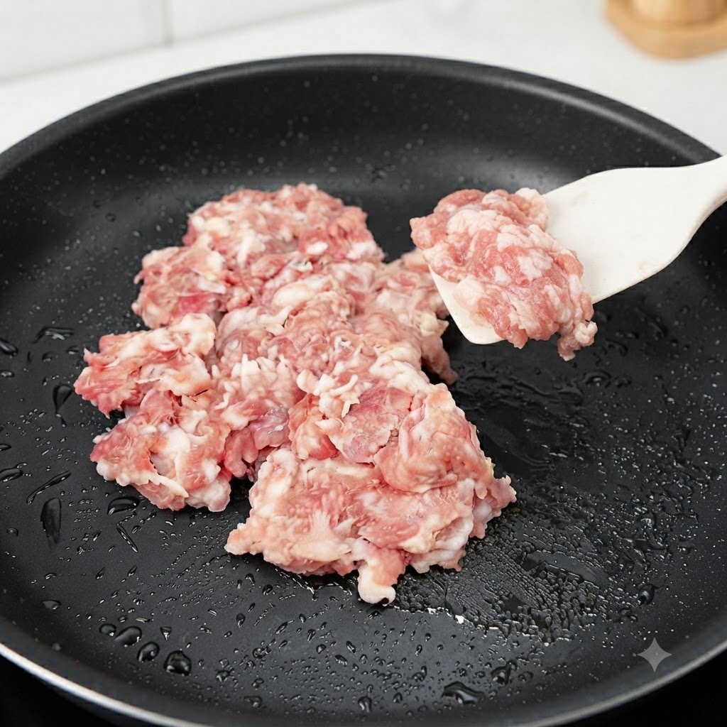 Carne di maiale macinata cruda aggiunta e saltata in una padella nera con una spatola in silicone.