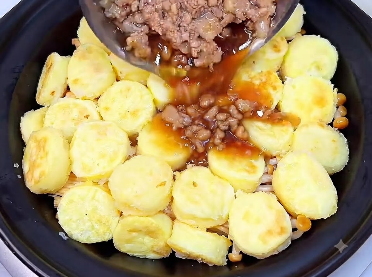 Maiale macinato cotto e salsa scura saporita versati da una padella sullo strato di tofu dentro il tegame di coccio.