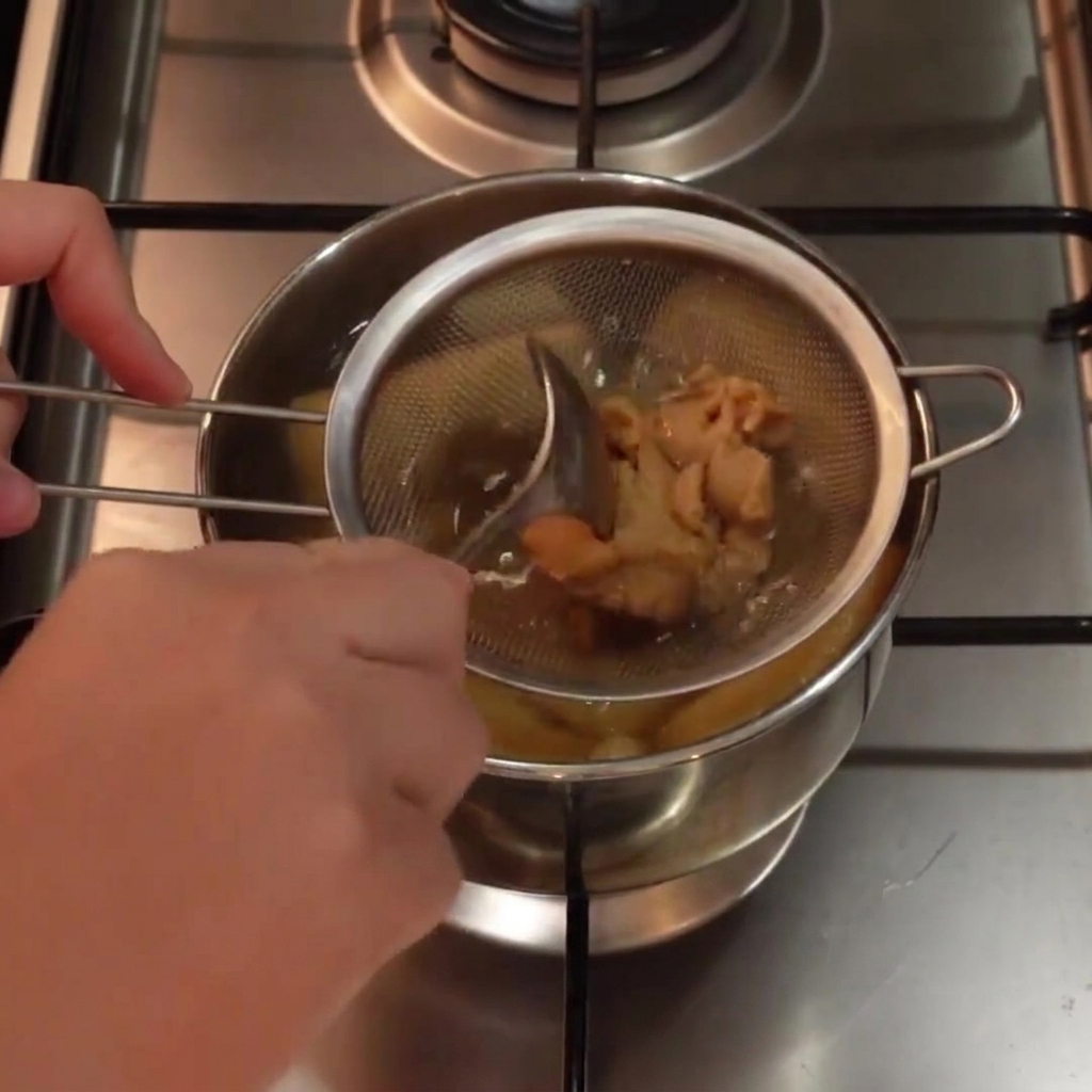 Pasta di miso bianco mescolata con un cucchiaio allinterno di un colino metallico immerso in una pentola di zuppa calda.