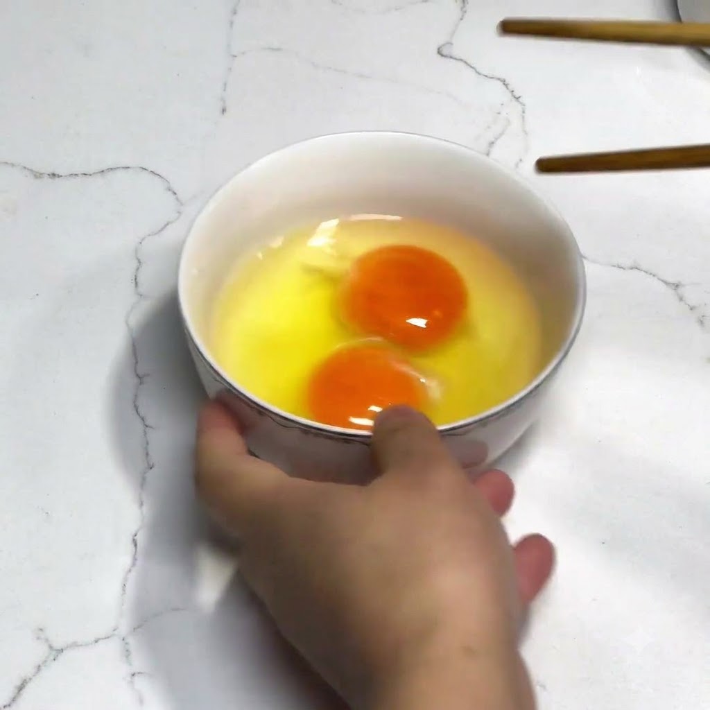 Due uova fresche in una ciotola bianca sbattute con bacchette di legno senza alcuna spezia.