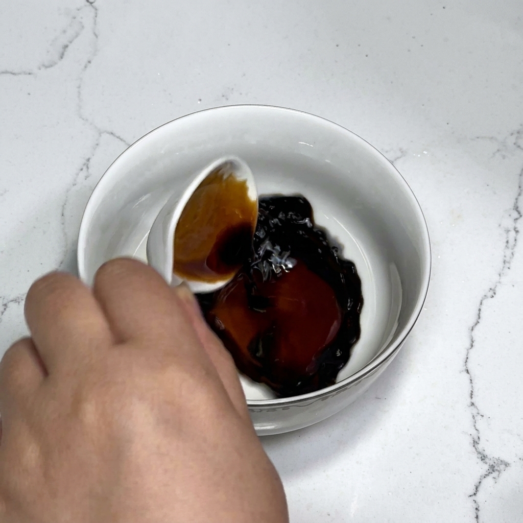 Ingredienti della salsa tra cui salsa di soia, salsa di ostriche, zucchero e amido mescolati con acqua in una ciotola bianca usando un cucchiaio.