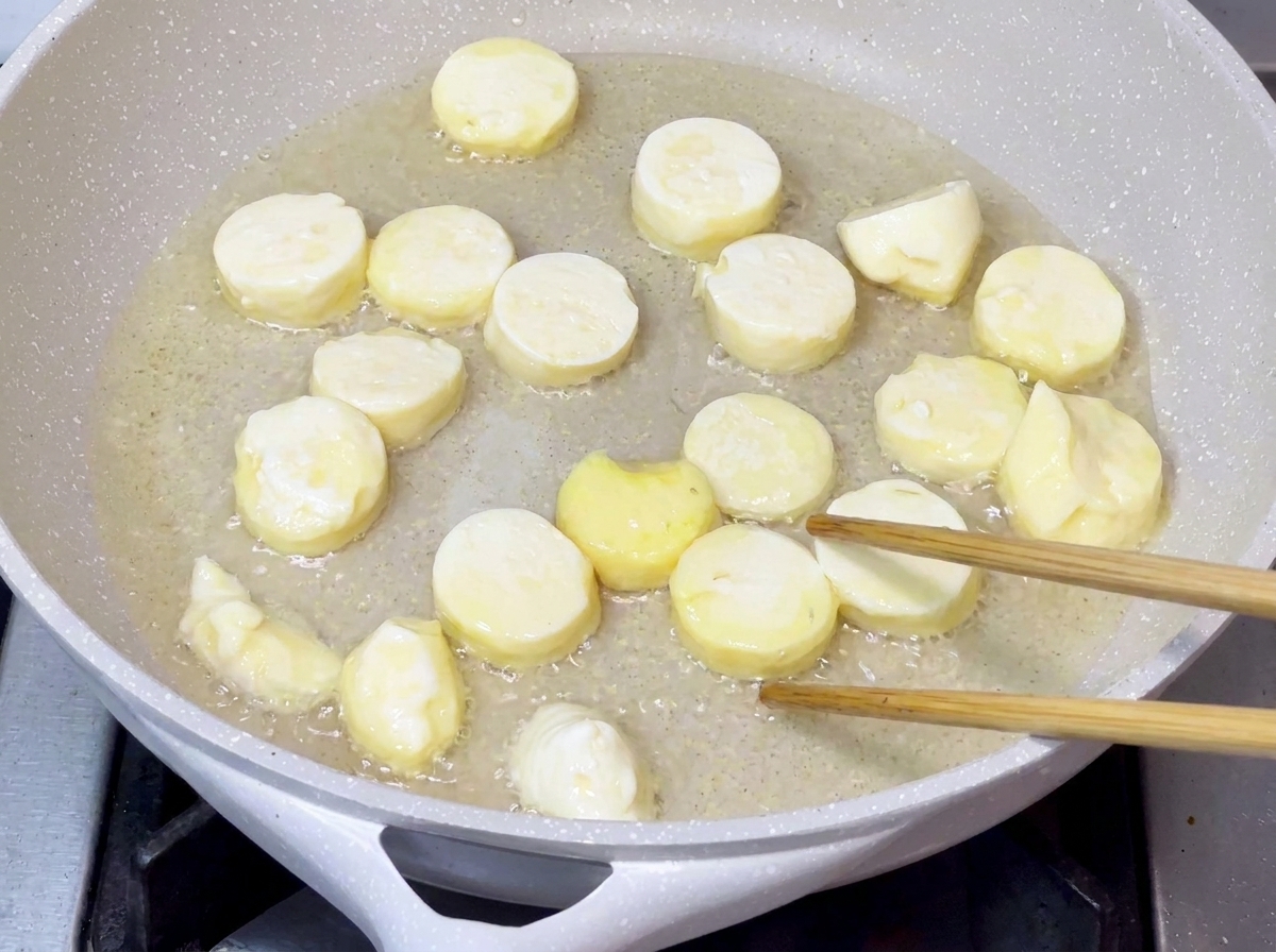 Pezzi di tofu che friggono in olio caldo in una padella finché le loro superfici non diventano dorate e croccanti.