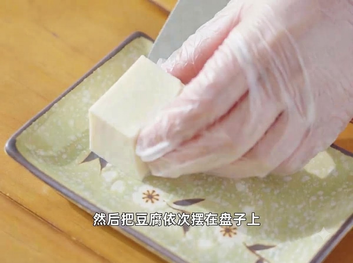 Mani guantate che dispongono un pezzo di tofu silken tagliato su un piatto verde decorativo.