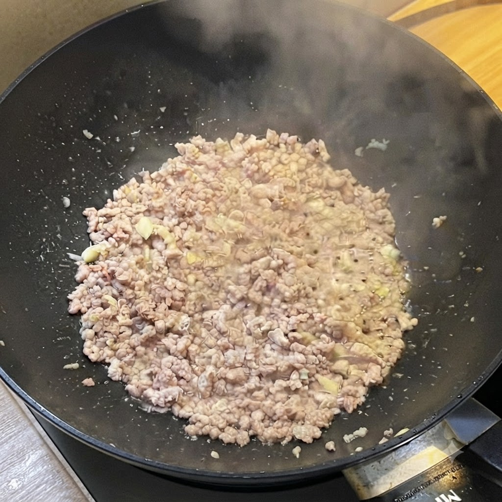 Un wok pieno di carne macinata rosolata che rilascia vapore mentre viene condita con salse liquide.