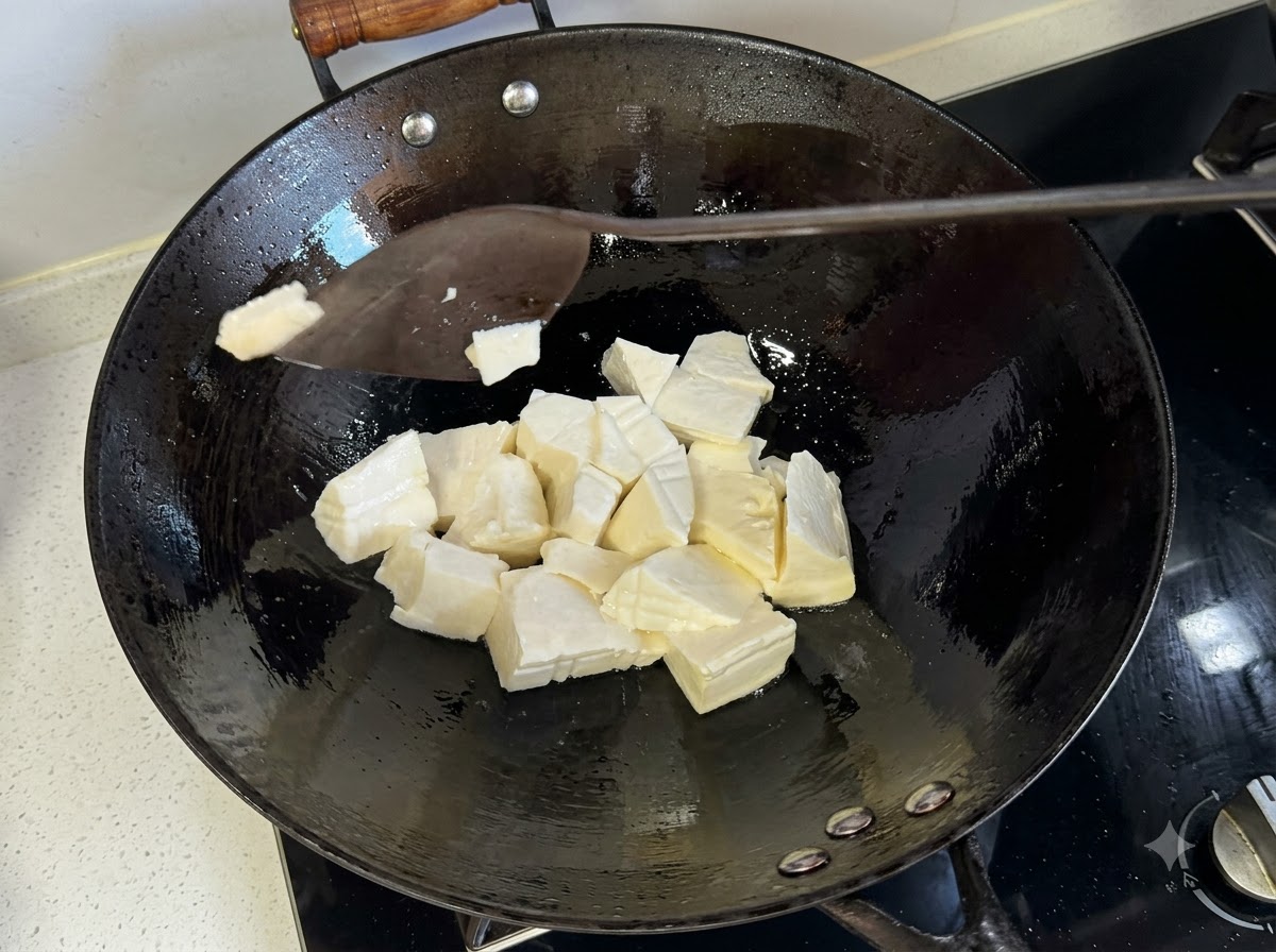 Una spatola che taglia pezzi di tofu morbido allinterno di un wok caldo.