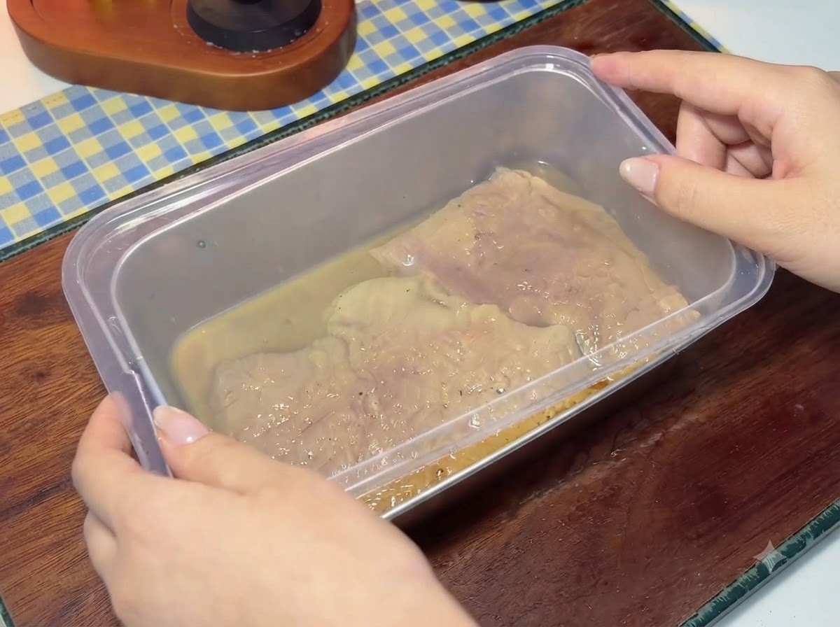 Un coperchio di plastica che viene posizionato saldamente su un contenitore pieno di cotolette di maiale marinate e liquido.