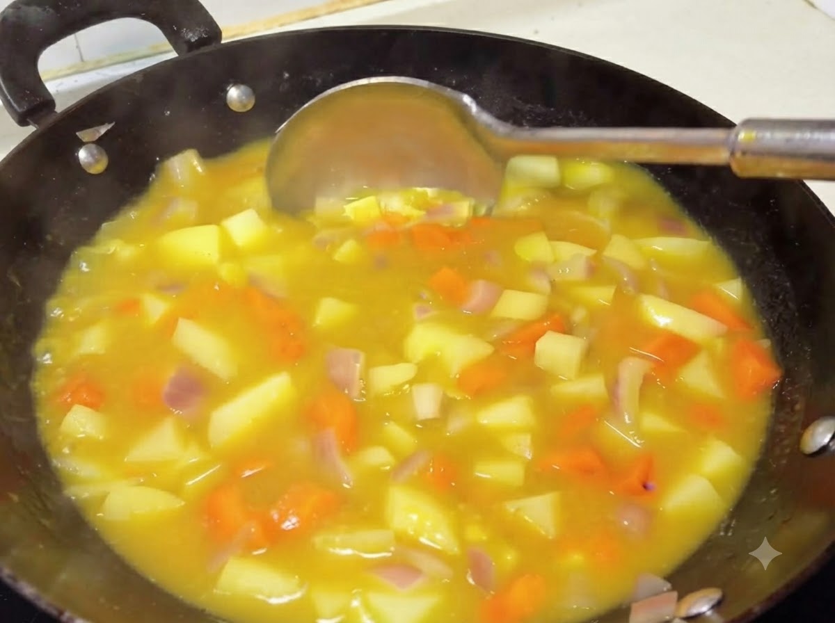 Un mestolo che mescola una densa e ricca salsa curry gialla con patate e carote in un wok.