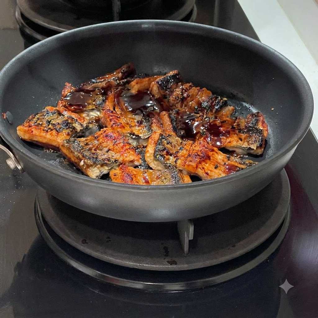 Salsa scura che viene fatta colare sopra i segmenti di anguilla sfrigolanti in una padella.