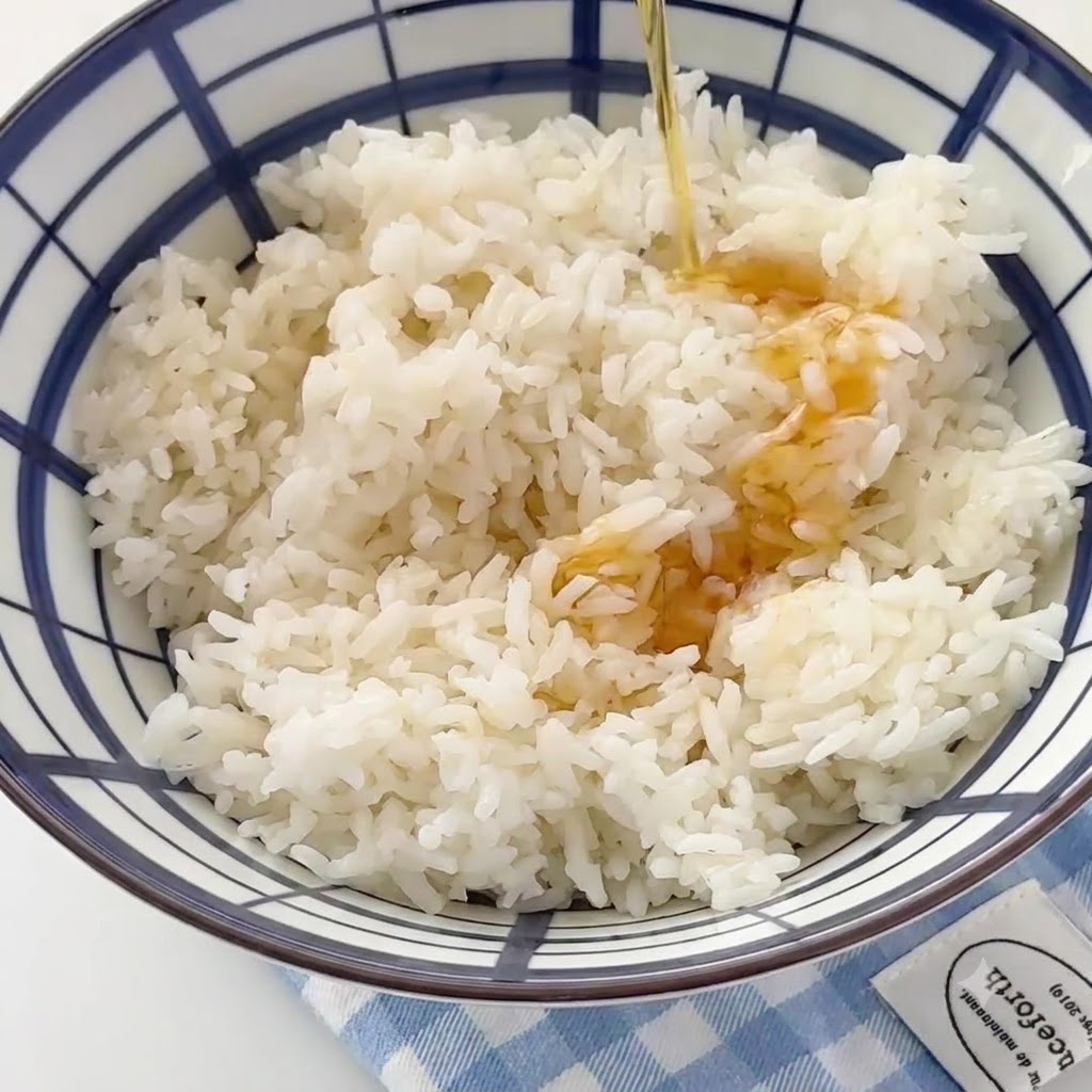 Olio di sesamo che viene versato a filo in una grande ciotola riempita di riso bianco cotto.