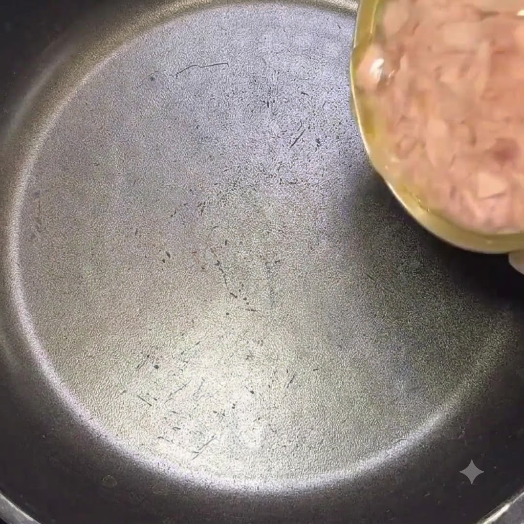 Una grande scatola di tonno versata con il suo olio in una padella nera.