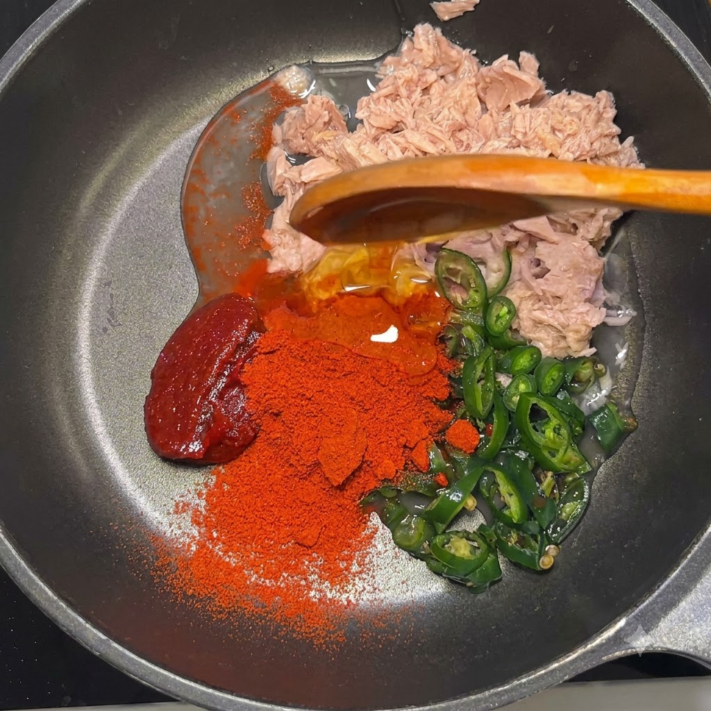 Pasta gochujang, polvere rossa di gochugaru, sciroppo di mais e maionese nella padella sopra il tonno e i peperoncini.