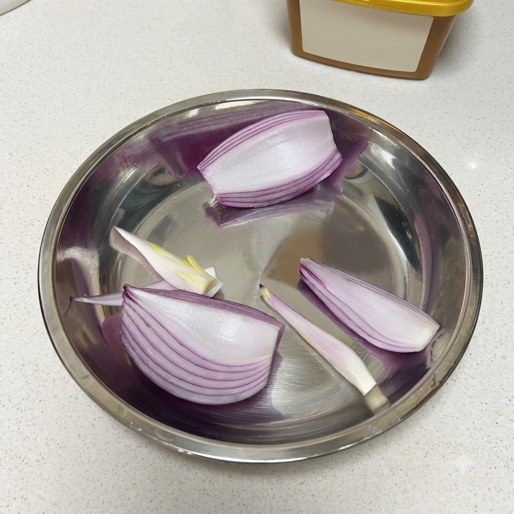 Cipolla rossa tagliata, mezza mela e spicchi daglio crudi sbucciati disposti allinterno di una ciotola di metallo.