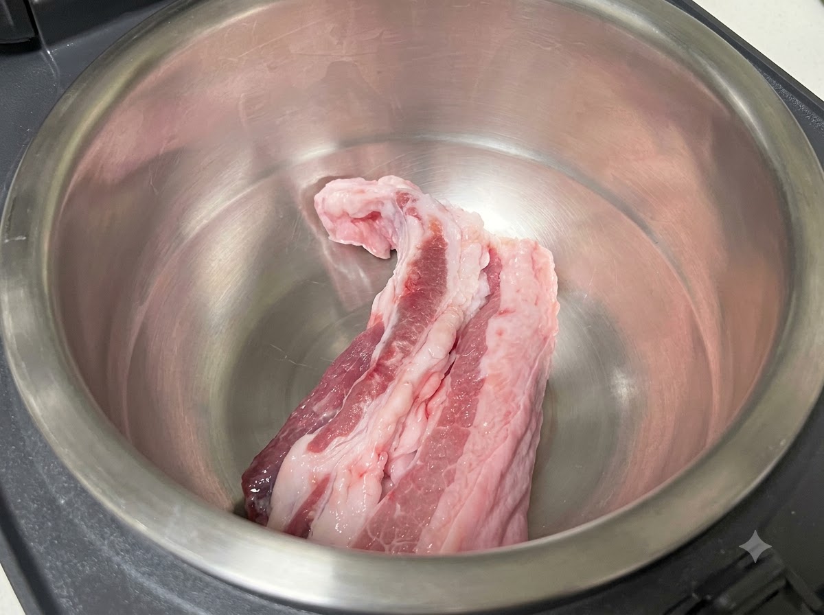 Strisce di pancetta di maiale cruda adagiate allinterno del contenitore interno in acciaio inossidabile di un cuociriso.