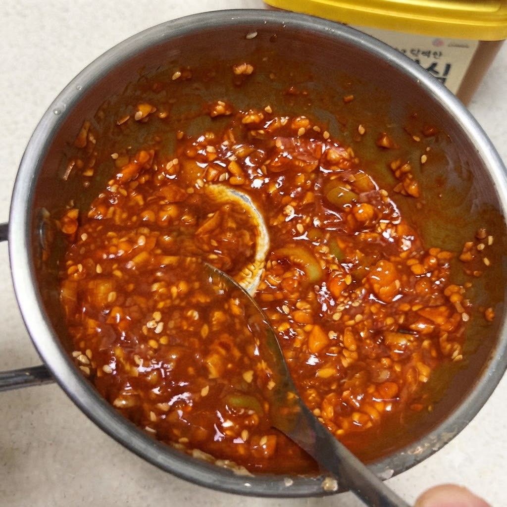 Un cucchiaio che mescola una densa e vibrante salsa di accompagnamento coreana rossa allinterno di una piccola padella di metallo.