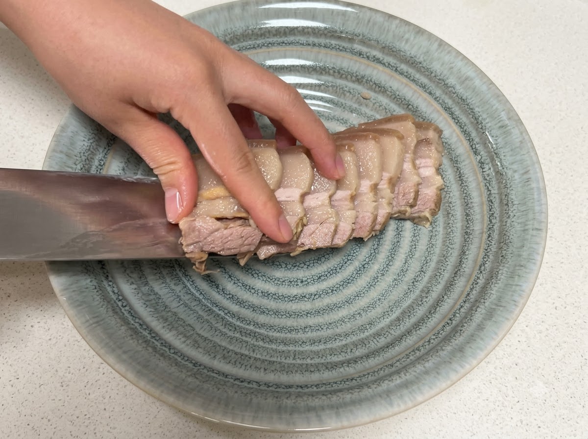 Fette di pancetta di maiale cotta trasferite su un piatto grigio strutturato con un coltello.