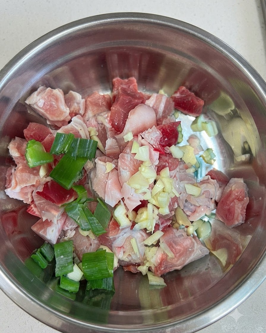 Pezzi crudi di pancetta di maiale in una ciotola uniti ad aglio, cipollotti e pasta di peperoncino rosso.