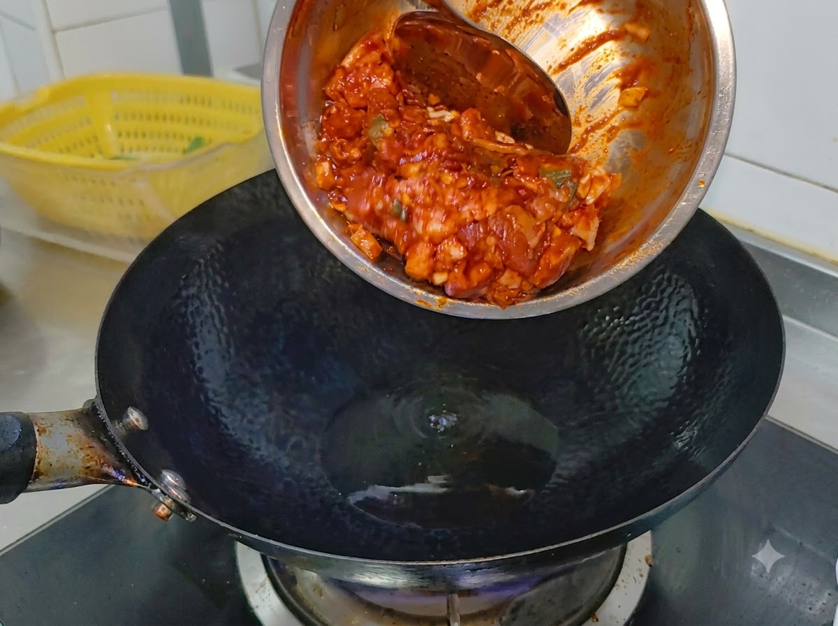 Pancetta di maiale piccante marinata che scivola da una ciotola di metallo in un wok nero rovente contenente olio da cucina.