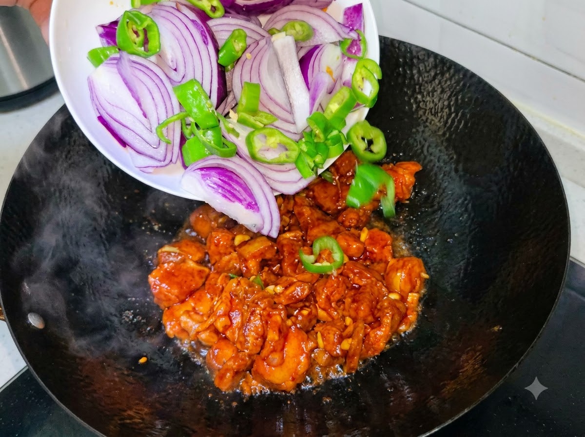 Fette di cipolla viola e peperoncini verdi versati da un piatto bianco in un wok con pancetta di maiale in cottura.