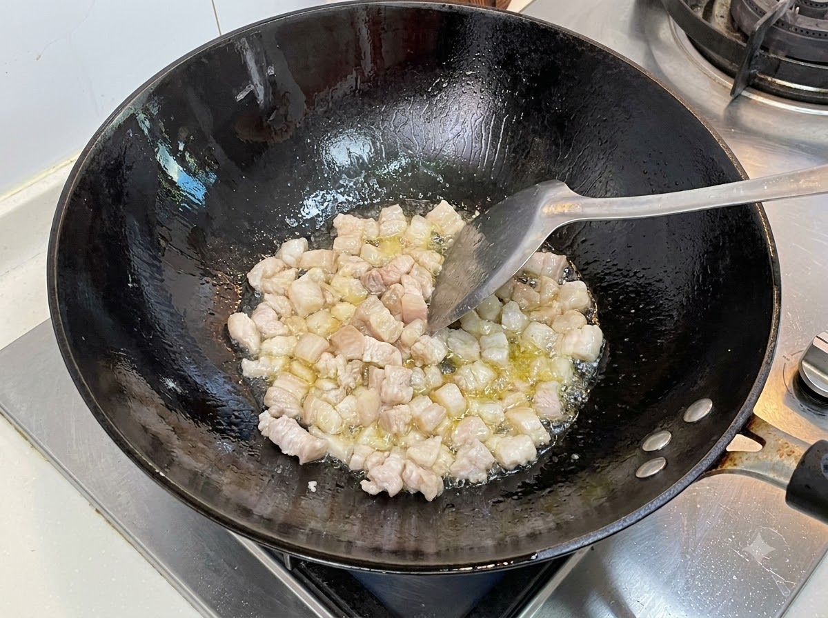 Cubetti di maiale grassi che friggono in un wok nero caldo con olio da cucina mescolato con una spatola.