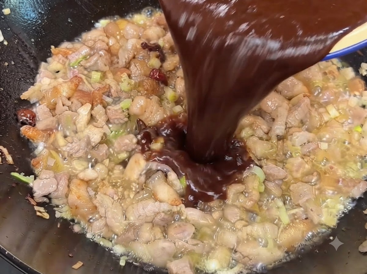 Miscela di salsa di soia scura e pasta di fagioli dolci versata nel wok sopra il maiale cotto.