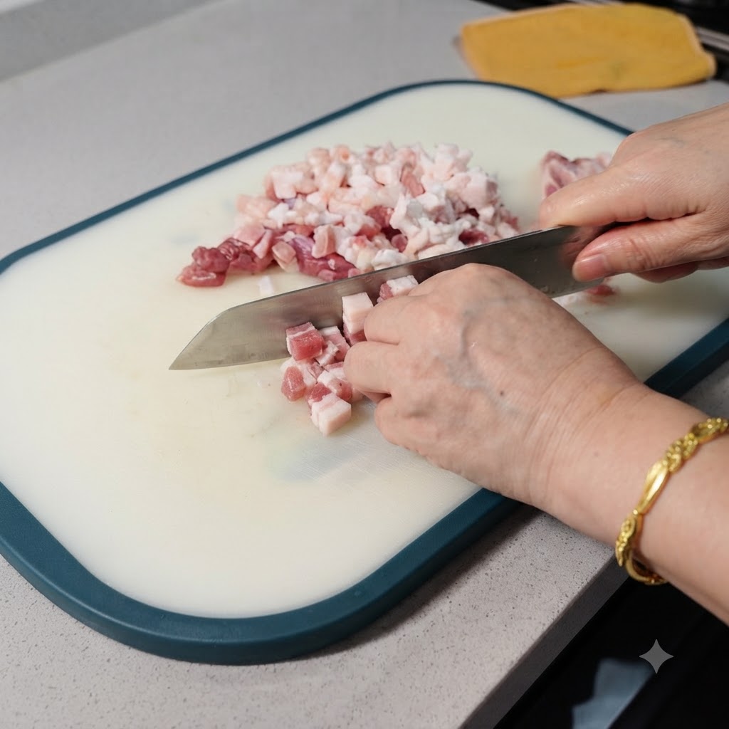 Una vista ravvicinata di pancetta di maiale cruda tagliata a piccoli cubetti con una mannaia su un tagliere bianco.