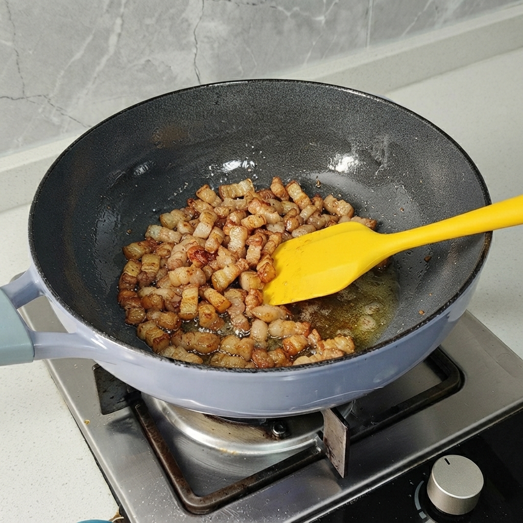 Pezzi di pancetta di maiale saltati in padella con una spatola gialla fino a doratura leggera.