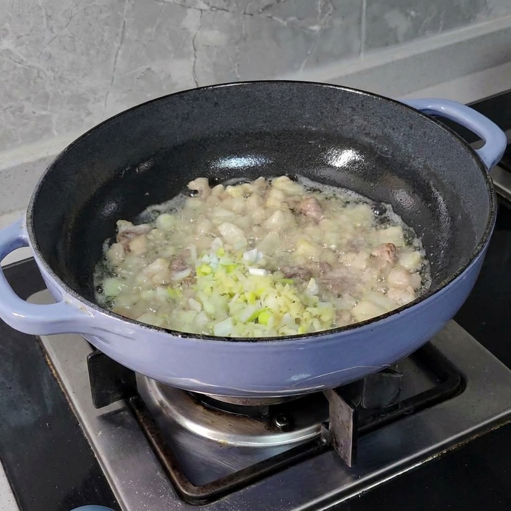 Cipollotti, zenzero e aglio tritati finemente aggiunti ai pezzi di maiale sfrigolanti in una padella scura.