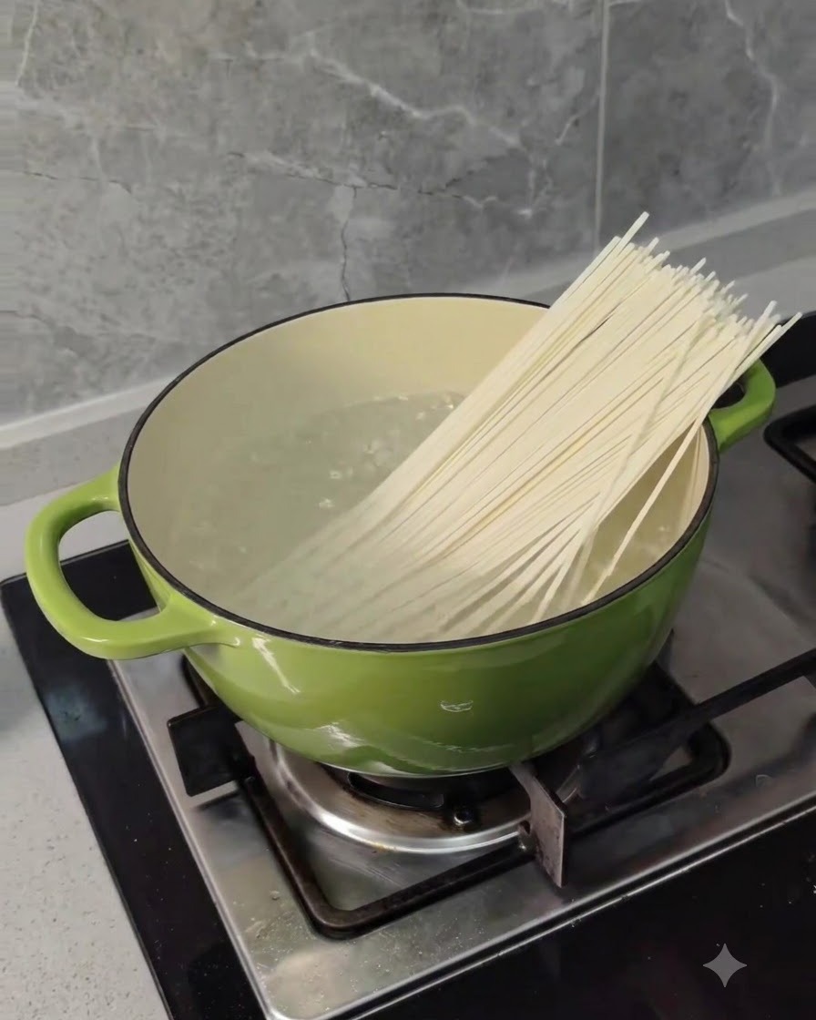 Noodles di grano lunghi secchi inseriti in una pentola verde di acqua bollente su un fornello.