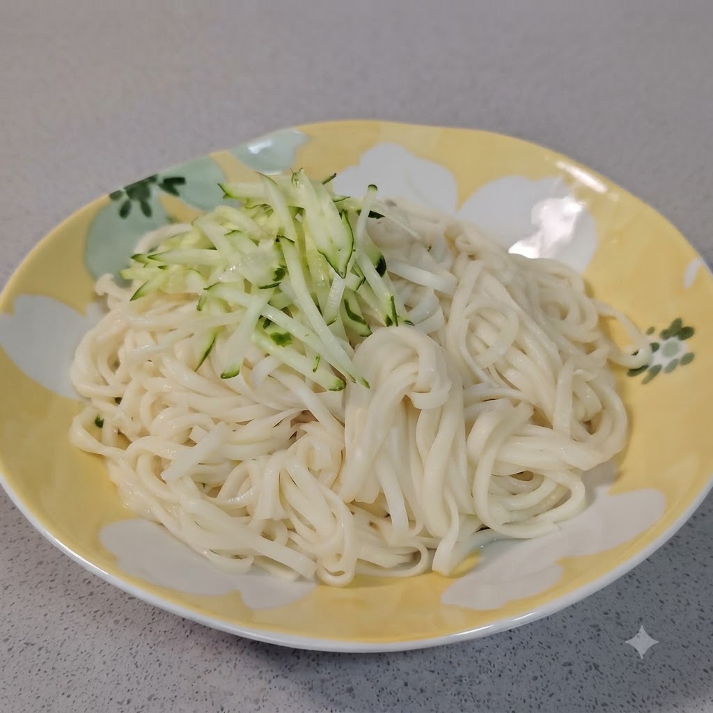 Un piccolo mucchio di cetriolo verde fresco tagliato a julienne posizionato sopra noodles bianchi bolliti in un piatto decorativo.