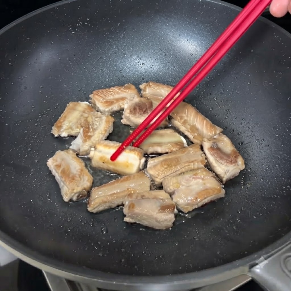 Costine di maiale che sfrigolano in una padella mentre vengono girate con le bacchette per dorarsi in modo uniforme.