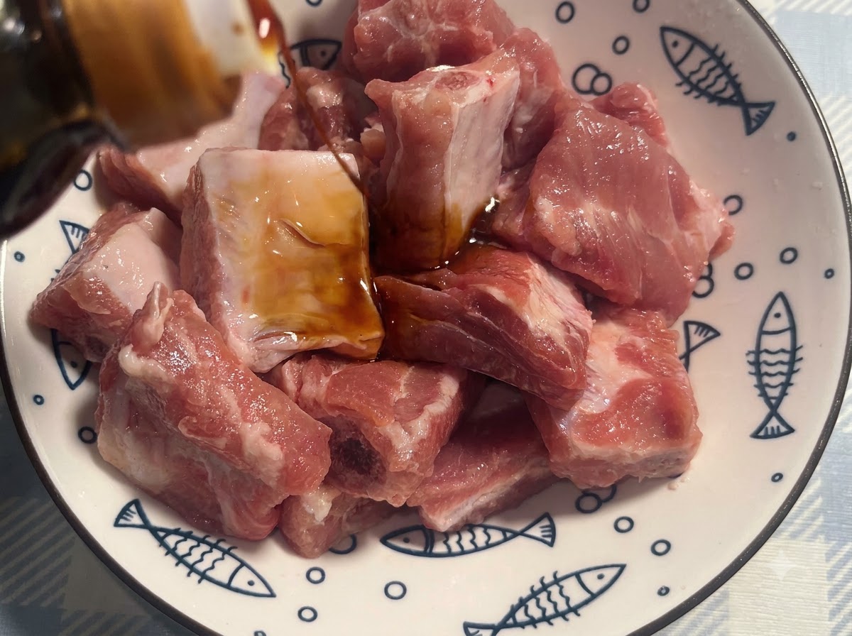 Costine di maiale in una ciotola bianca decorata condite con salsa di soia scura.